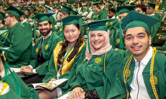A group of people wearing green graduation caps and gowns. Description generated by AI