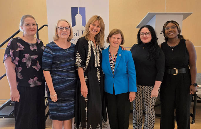 A group of women standing in front of a podium. Description generated by AI