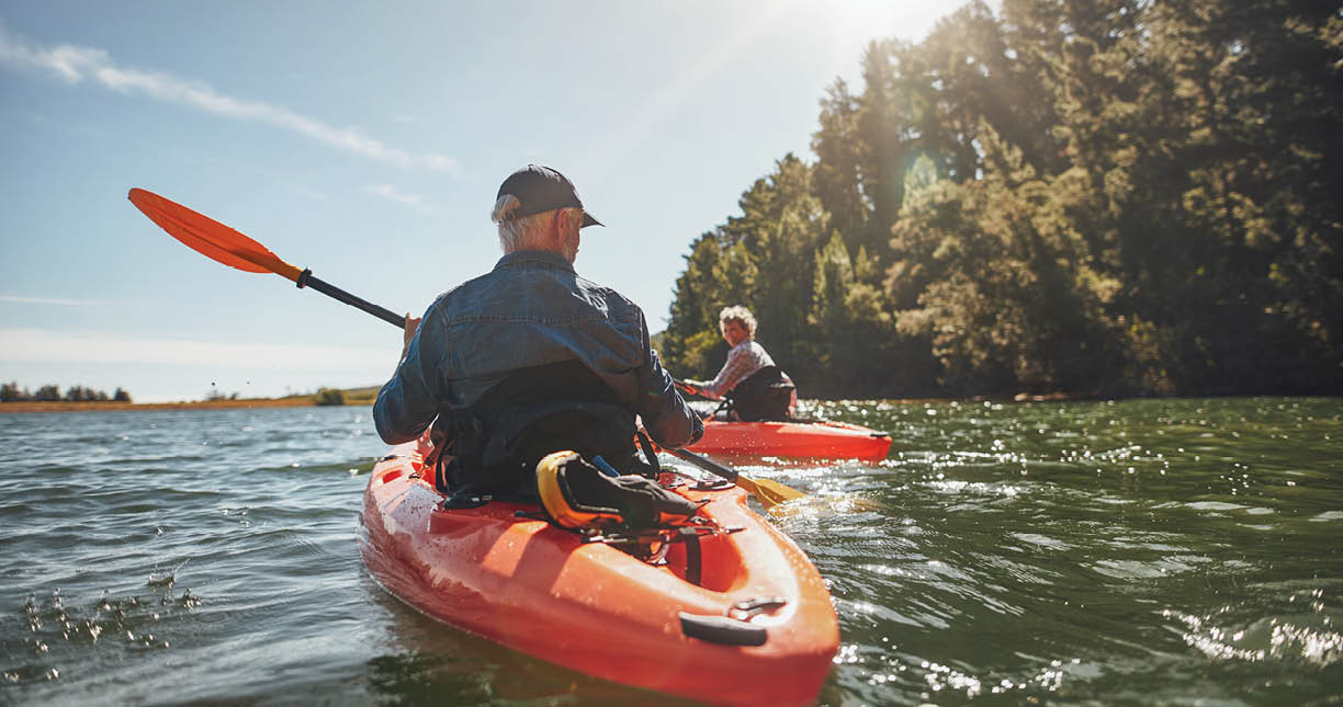 Outdoor shot of mature man canoeing in the lake with woman in background. Couple kayaking in the lake on a sunny day.