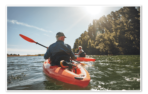 Outdoor shot of mature man canoeing in the lake with woman in background. Couple kayaking in the lake on a sunny day.
