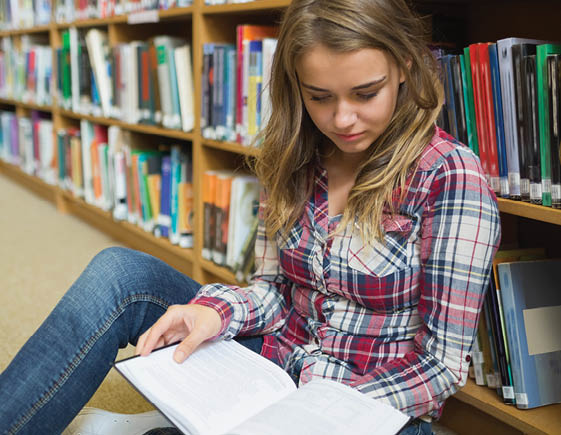 Young pretty student sitting on library floor reading book in college