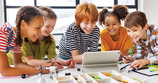 Positive kids pupils schoolchildren    happy smiling and   looking at tablet screen during study scheme of assembly of robots during collective school work in light classroom