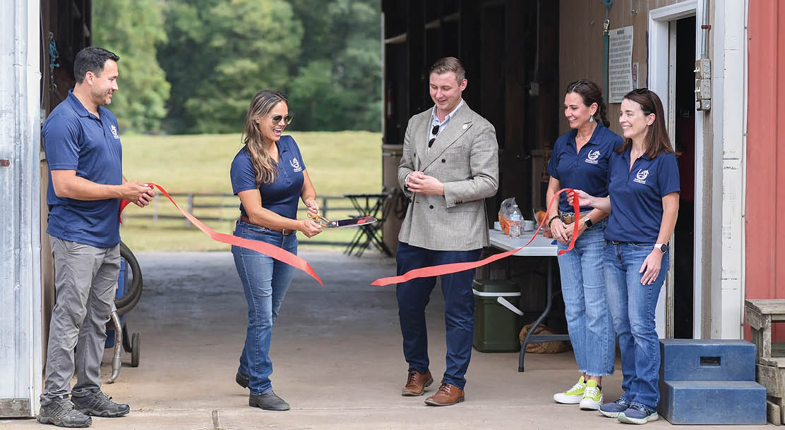 A group of people are standing in a garage, with a man holding a red ribbon. The people are wearing blue shirts and are in the process of cutting the ribbon. AI generated content