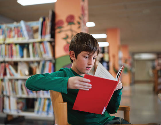 Boy reading a red book in a library