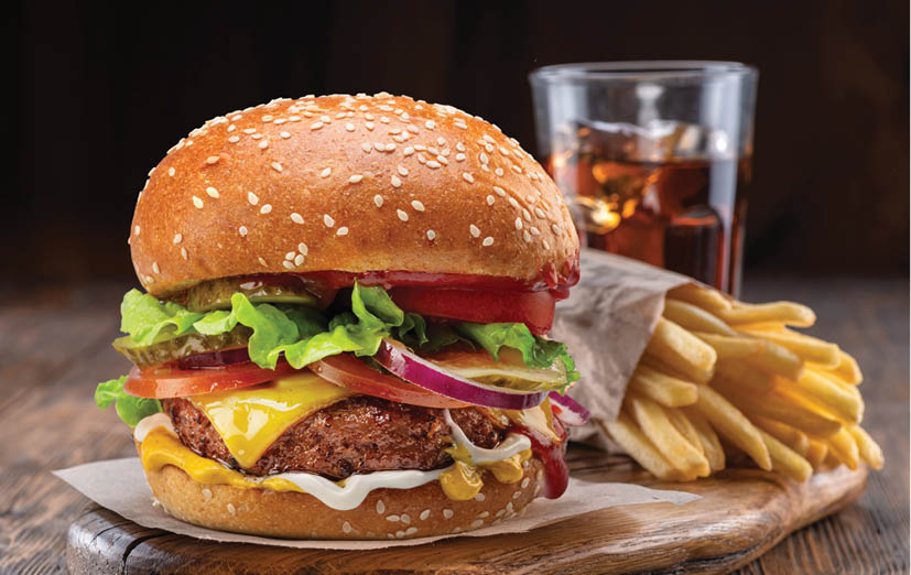 Tasty cheeseburger or hamburger, glass of cola and french fries on wooden tray close-up.