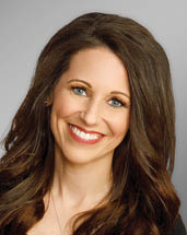 A woman with long brown hair sitting on a white chair. Description generated by AI