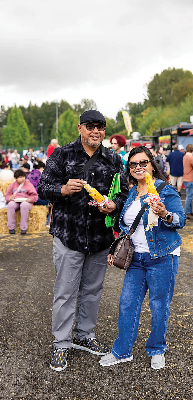 A man and woman are standing on the street eating corn on the cob. Description generated by AI