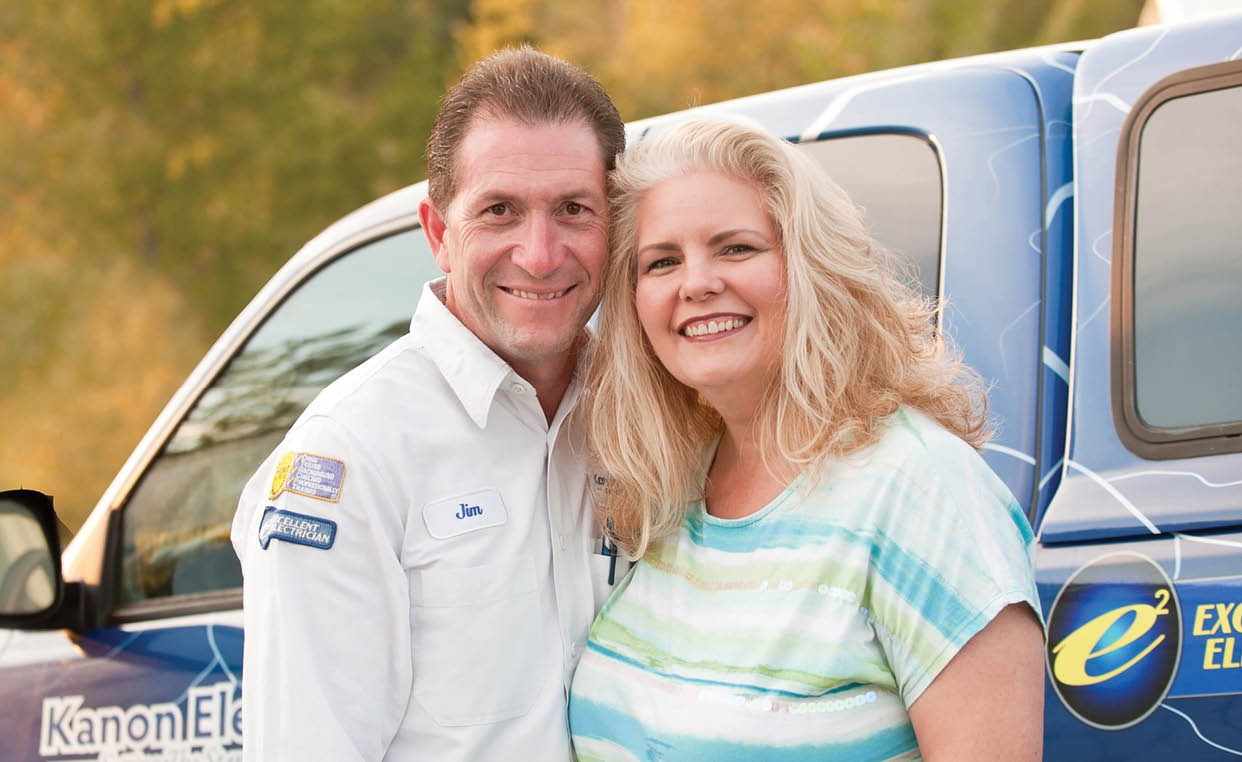 A man and woman standing in front of a blue truck. Description generated by AI
