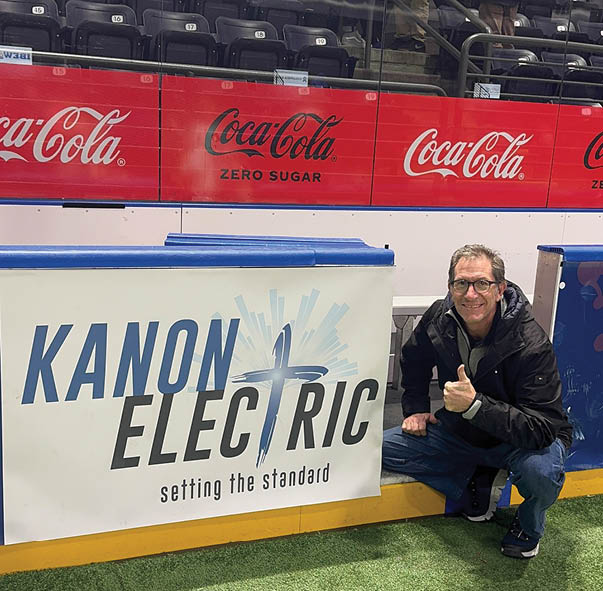 A man is kneeling in front of a sign that says Kanon Electric. Description generated by AI