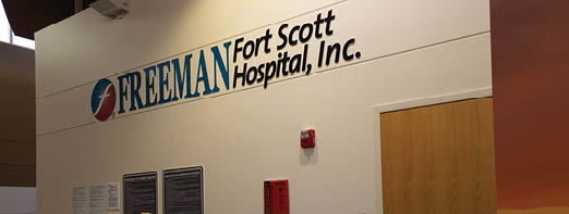 A vase of flowers sits on a desk in a room with a sign that says “Fort Scott Hospital Inc.". AI generated content