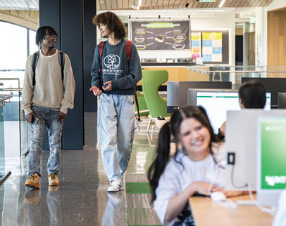 A group of people are in a room with computers. A man and a woman are walking by a table with a laptop on it. AI generated content