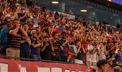 A large crowd of people are sitting in the stands, watching a game. They are all holding up their hands, showing their excitement and support for the players. AI generated content