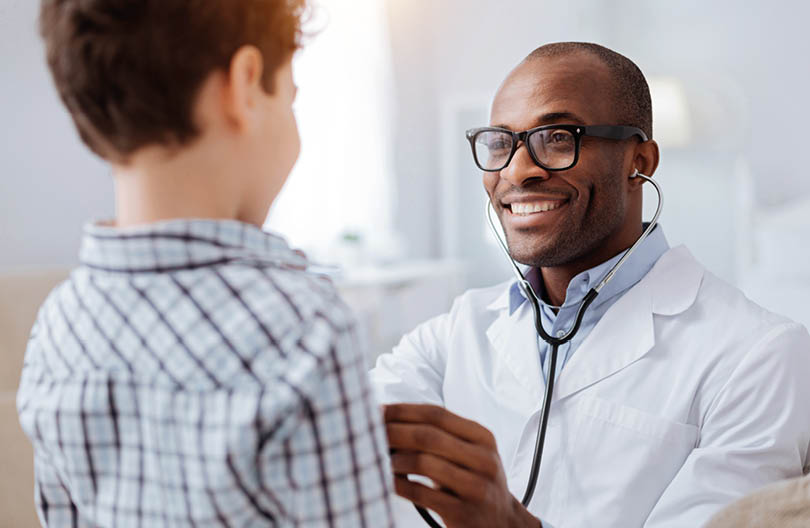 Stethoscope exam. Attractive cheerful male doctor listening to boy while putting on glasses and using stethoscope