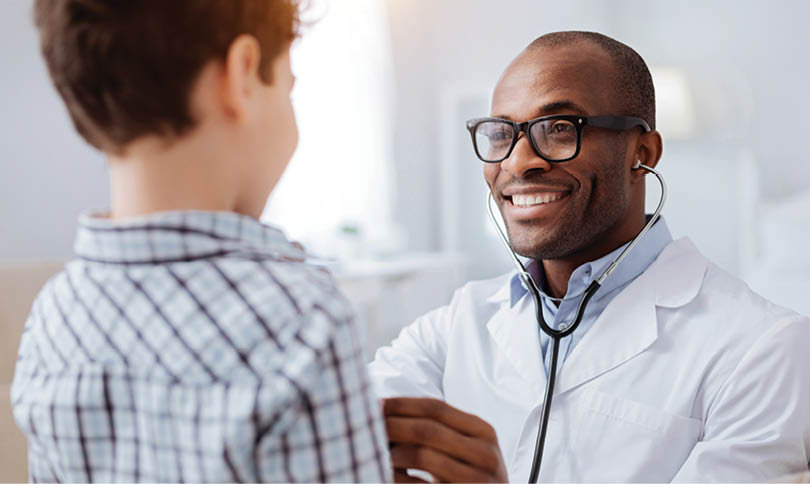 Stethoscope exam. Attractive cheerful male doctor listening to boy while putting on glasses and using stethoscope