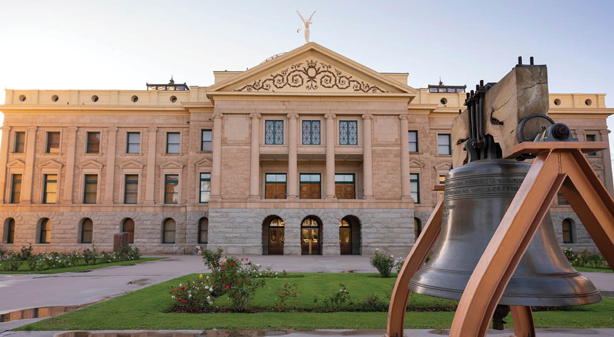 An old watchtower bell is mounted on the sidewalk in front of the state capitol building in Phoenix AZ