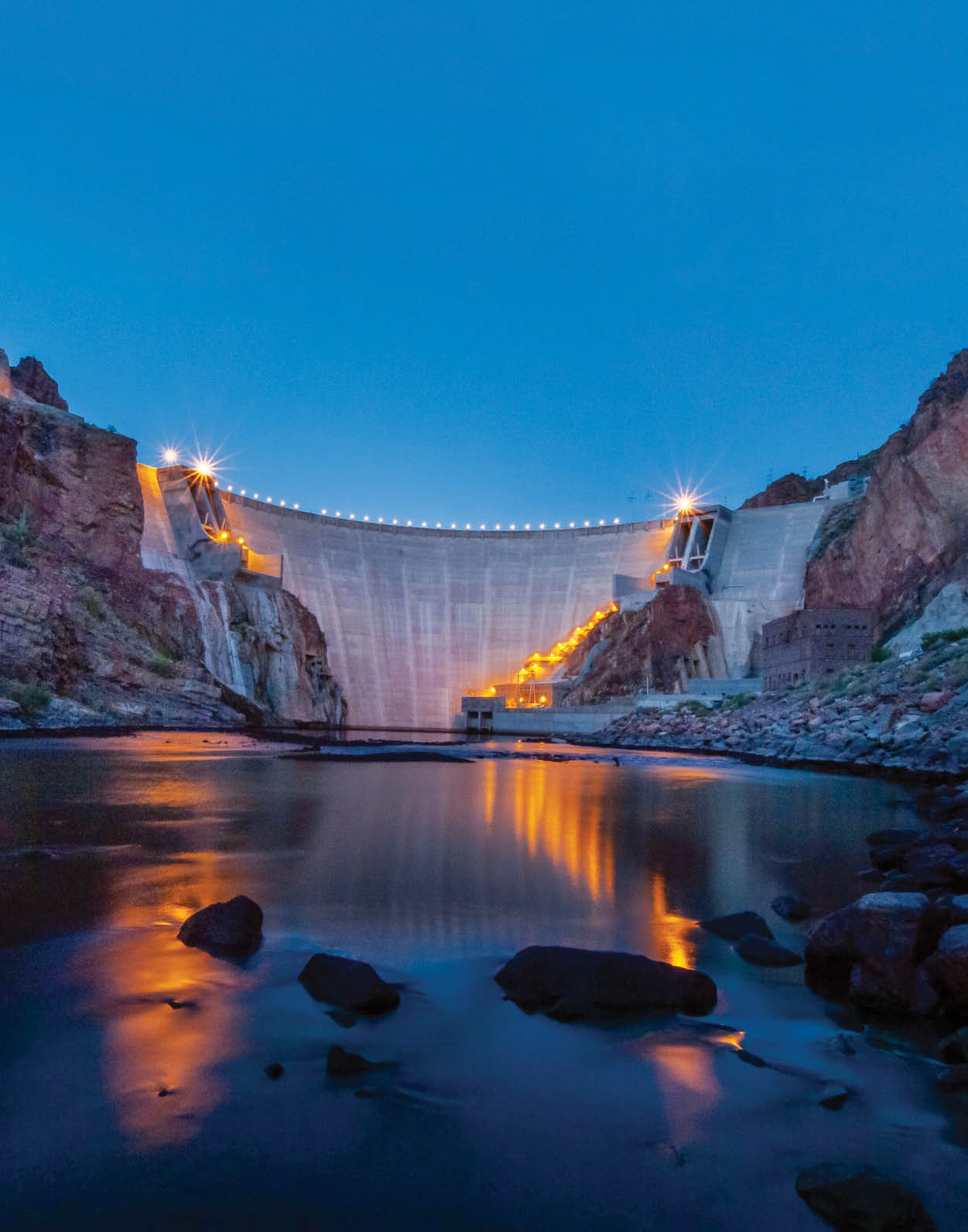 Roosevelt Dam, low on the water, looking up at dam face, dusk or evening with lights