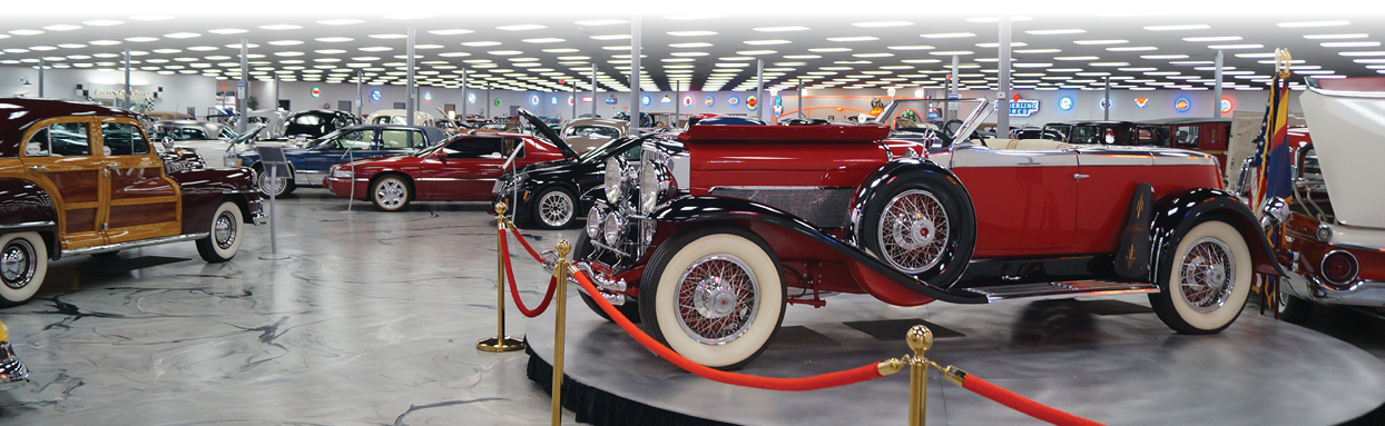 A large indoor space showcases various antique cars and trucks on display. The vehicles are arranged in a circular fashion, with some cars and trucks positioned in the center of the room. The display is likely part of a museum or exhibition, showcasing the history and evolution of automotive design. AI generated content