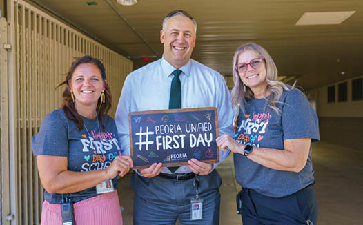 Three people pose for a picture, two women and a man, all wearing name tags. The man is holding a sign that says “Pedro Untied First Day." AI generated content