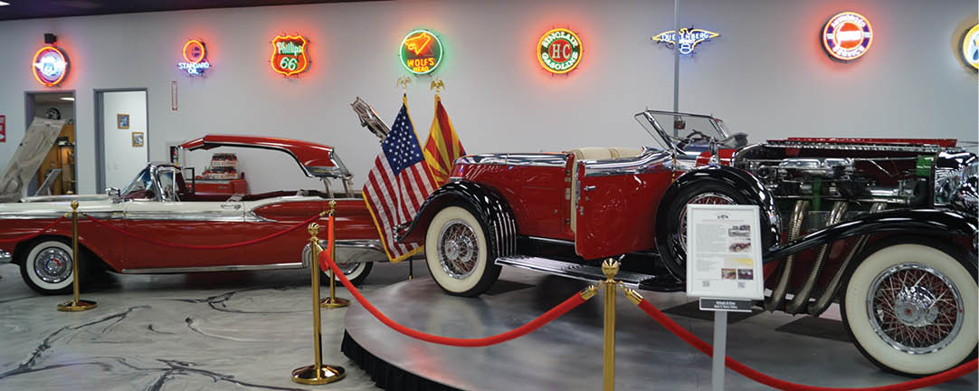 A red vintage car is on display in a museum, surrounded by other classic cars. The car has a flag on the front and is on a round platform. AI generated content