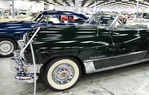 A black classic car is on display in a showroom, surrounded by other cars. AI generated content