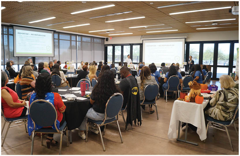 A group of people are sitting around a large table in a room. There are several chairs placed around the table, and a man is standing at the front of the room, giving a presentation. The people are engaged in the presentation, and there are cups and a bottle on the table. AI generated content