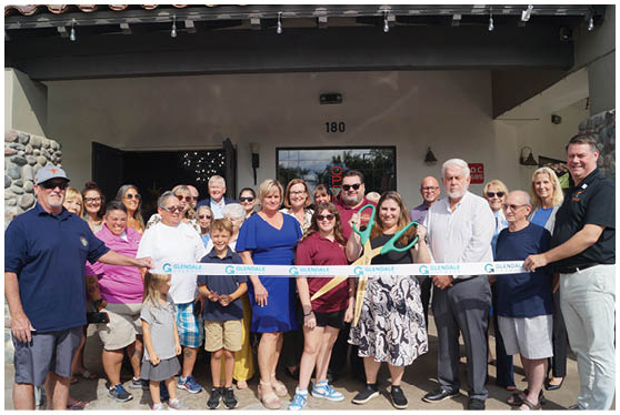 A group of people are standing in front of a building, posing for a picture. They are holding a ribbon, which is being cut by a man in a suit. The people are of various ages and are standing close to each other. AI generated content