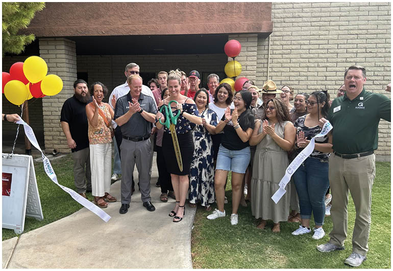 A group of people are gathered outside a building, with a man holding a pair of scissors. A woman is holding a ribbon, and the group is clapping. AI generated content
