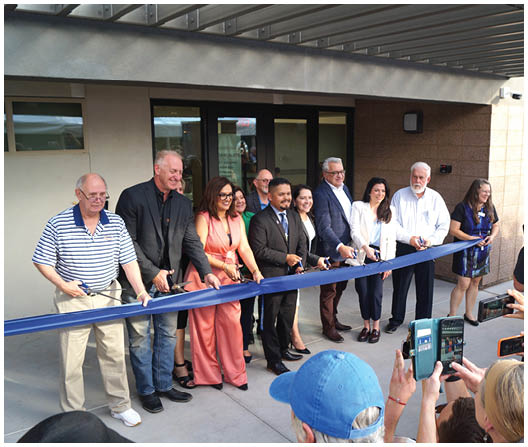 A group of people are gathered in front of a building, cutting a blue ribbon with a pair of scissors. They are posing for a photo. AI generated content