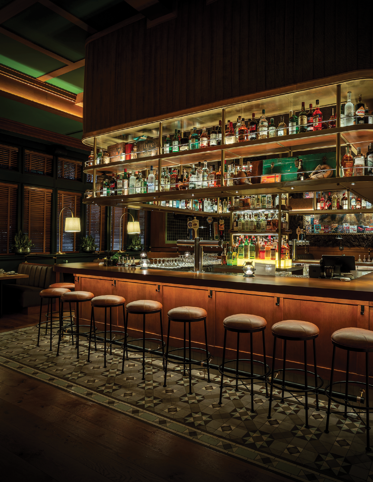 A bar with a long wooden counter and a row of stools. Description generated by AI