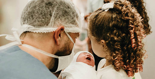 A man wearing a blue shirt is holding a baby. Description generated by AI