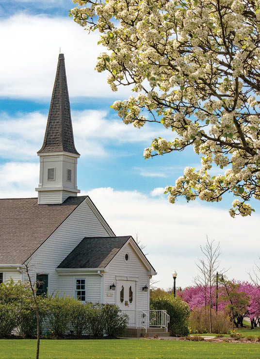 A white church with a steeple and a tree in front of it. Description generated by AI