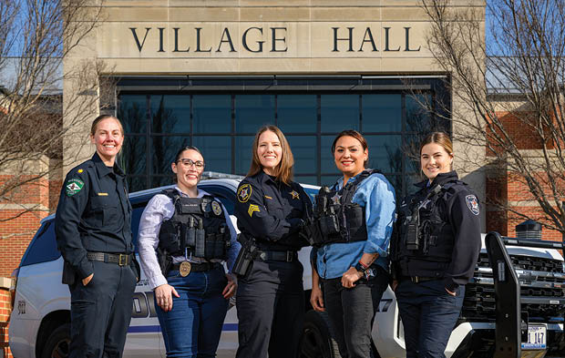 Five police officers standing in front of a building. Description generated by AI