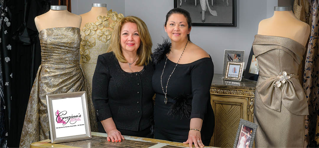 Two women standing in front of a display of dresses. Description generated by AI