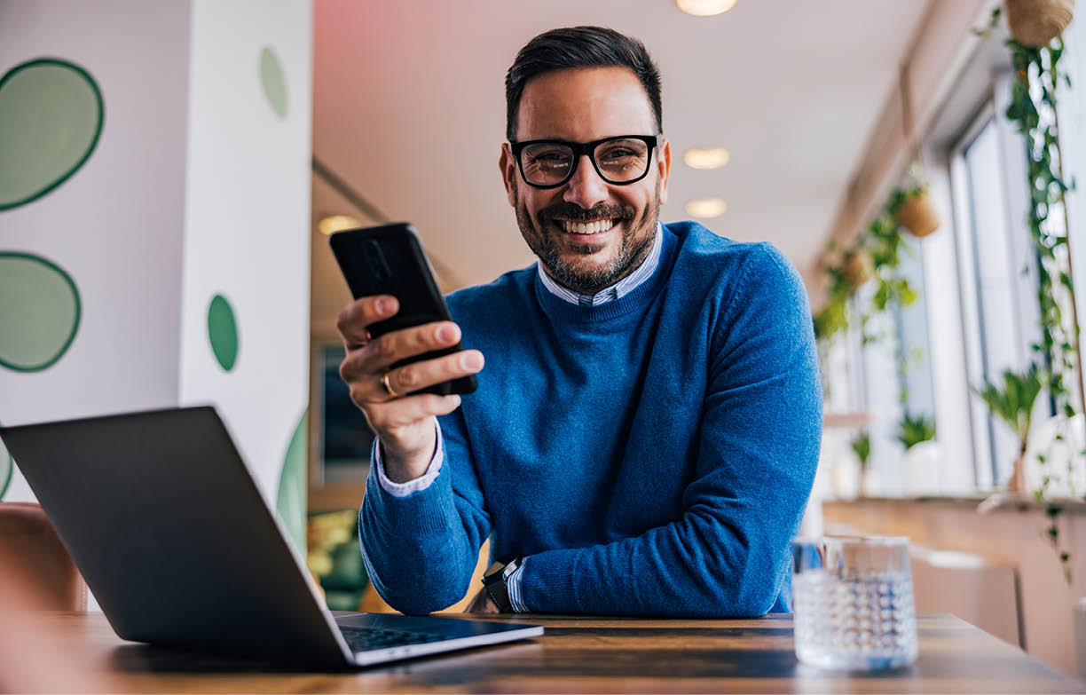 Cheerful businessman using a mobile phone, while working over the laptop at the office.