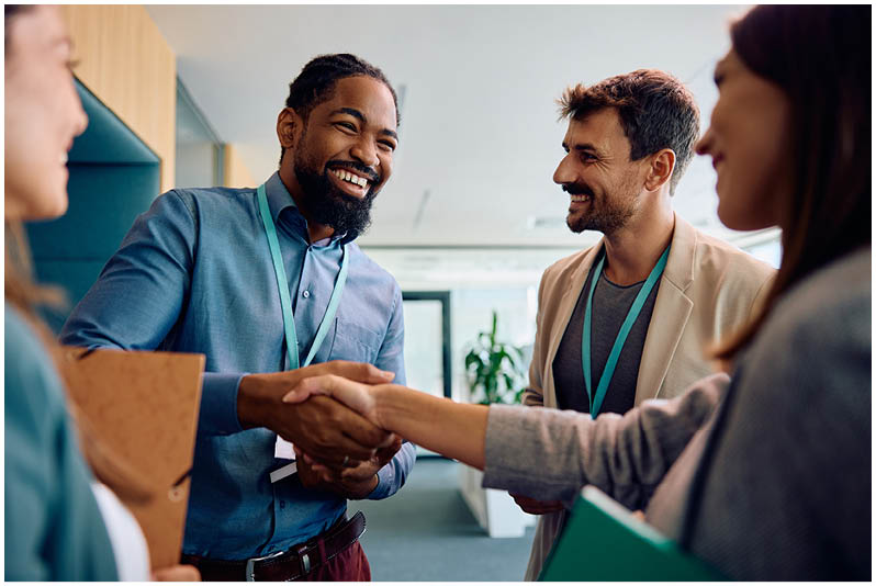 Group of coworkers greeting in the office. Focus is on African American businessman shaking hands with female colleague.