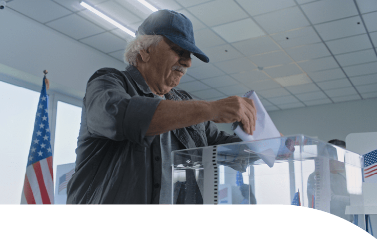 Elderly Caucasian man puts bulletin paper in box. Multiethnic American people and voters vote in voting booths at polling station. Unites States presidential elections. Election coverage. Patriotism.