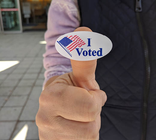 Voter holding up an I voted sticker on the thumb