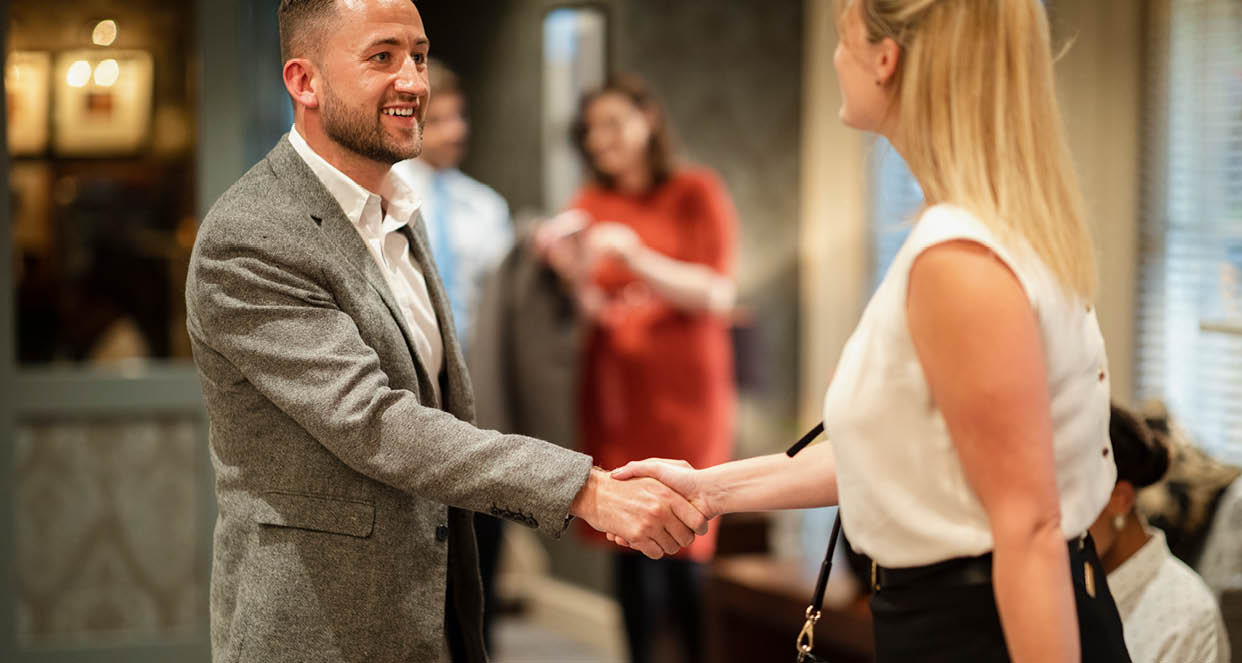 A shot of businessmen and businesswomen arriving in a lobby, they are greeting eachother with a handshake.