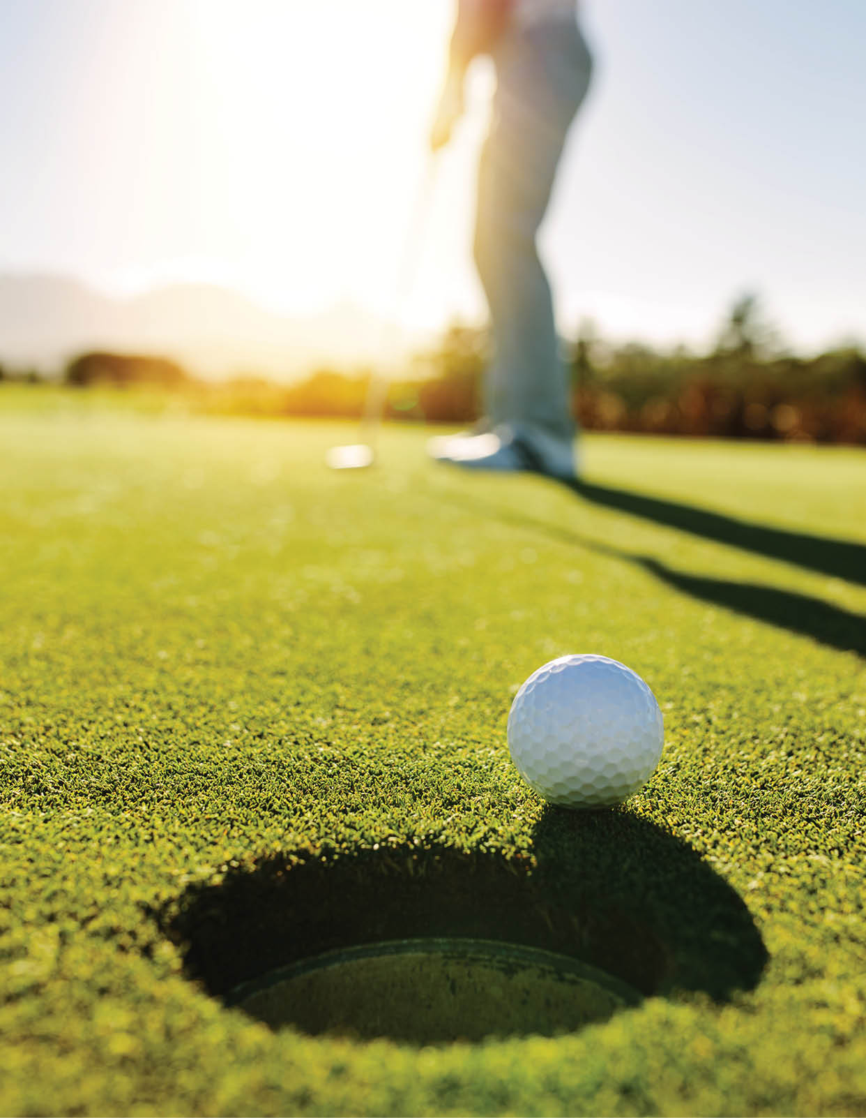 Golf ball at the edge of hole with player in background. Professional golfer putting ball into the hole on a sunny day.