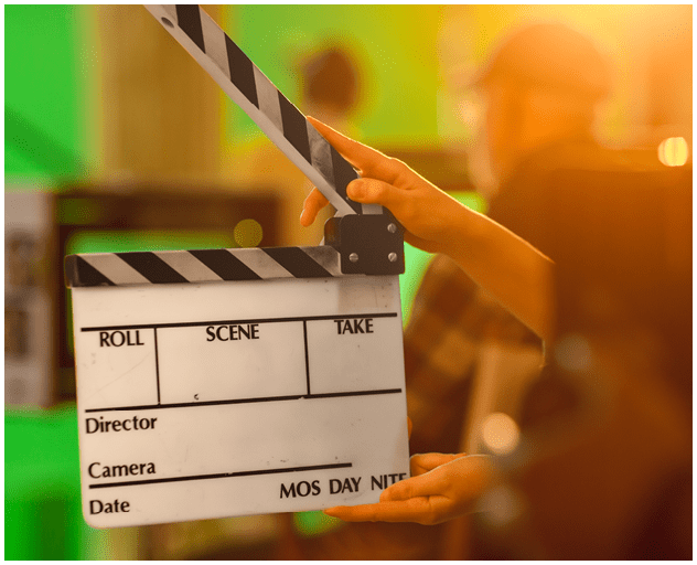 Close up Shot On Film Studio Set Young Camera Assistant Holds Empty Clapperboard. In the Background Director Shooting Green Screen Scene. History Costume Drama Movie.