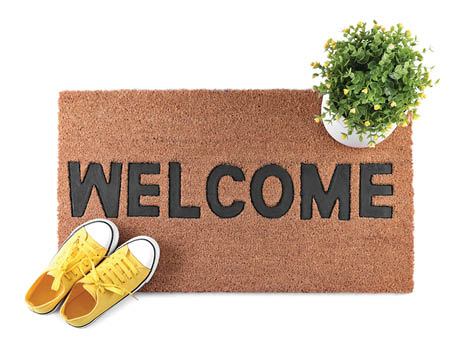 Stylish door mat with word Welcome, houseplant and shoes on white background, top view