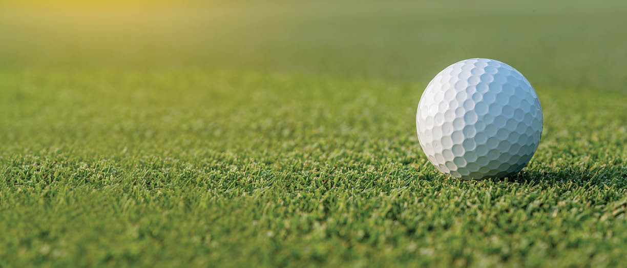 White golf ball on golf pin green grass near hole with golf course background , green tree sun ray
