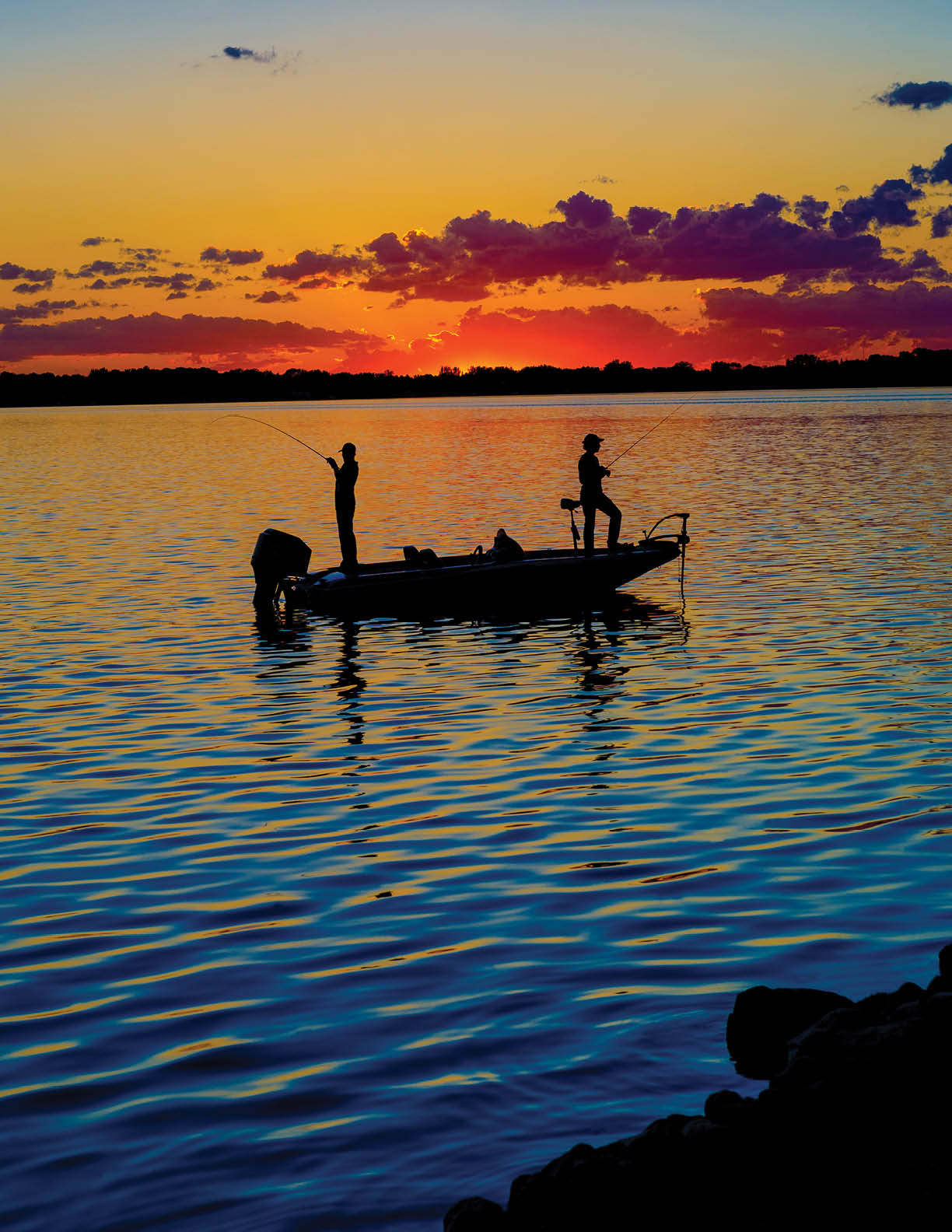 Fisherman in a boat at sunset with vibrant colors.