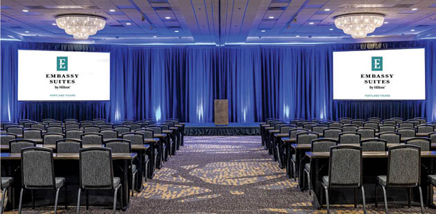 A large room with a blue carpet and a large screen. Description generated by AI