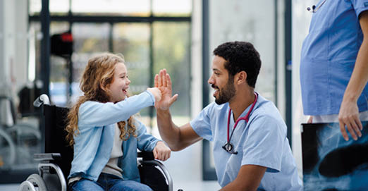 Young multiracial doctor having fun with little girl on a wheelchair.