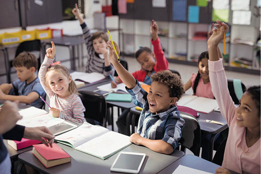 Schoolkids raising their hands in classroom at school