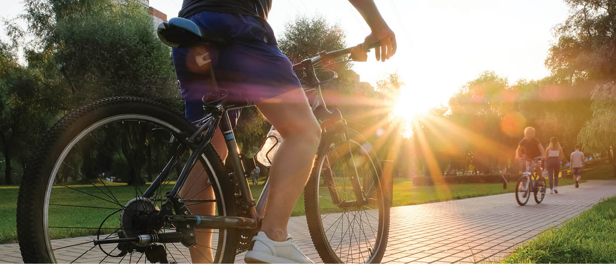 Man rides a bike outdoors in the park on a sunny day at sunset.