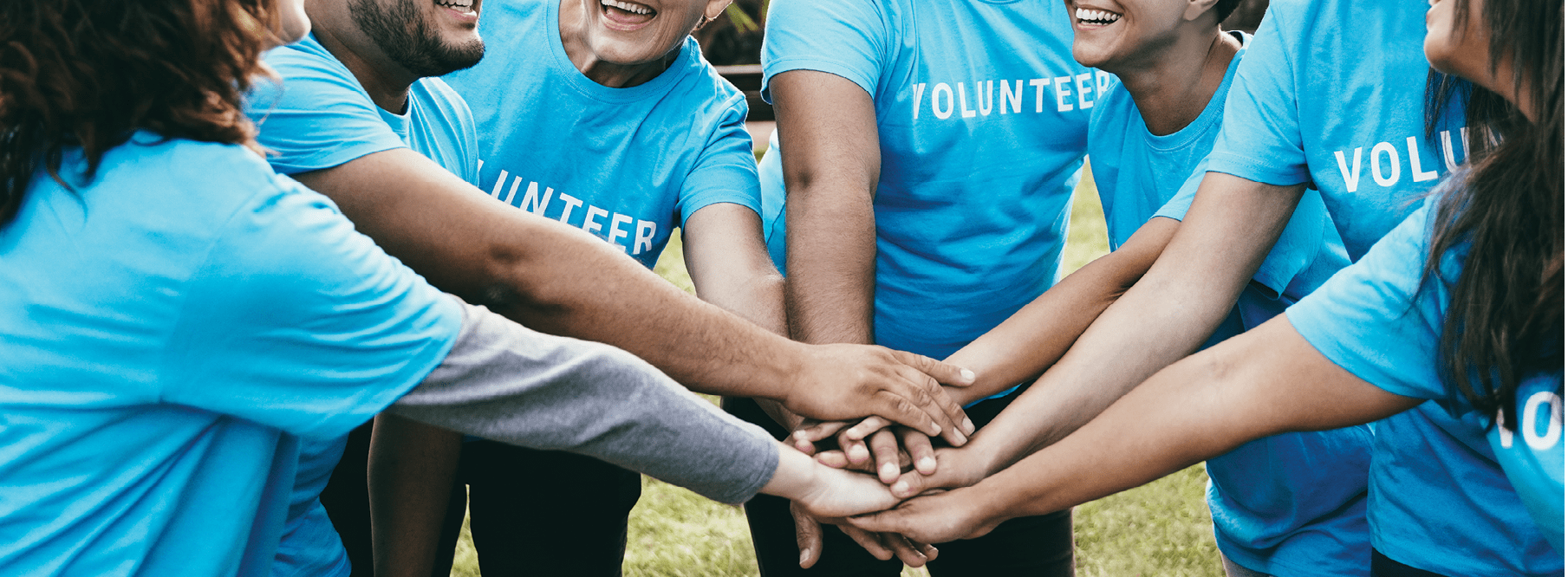Happy group of volunteer people stacking hands celebrating together outdoor - Teamwork and charity support concept - Focus on back faces