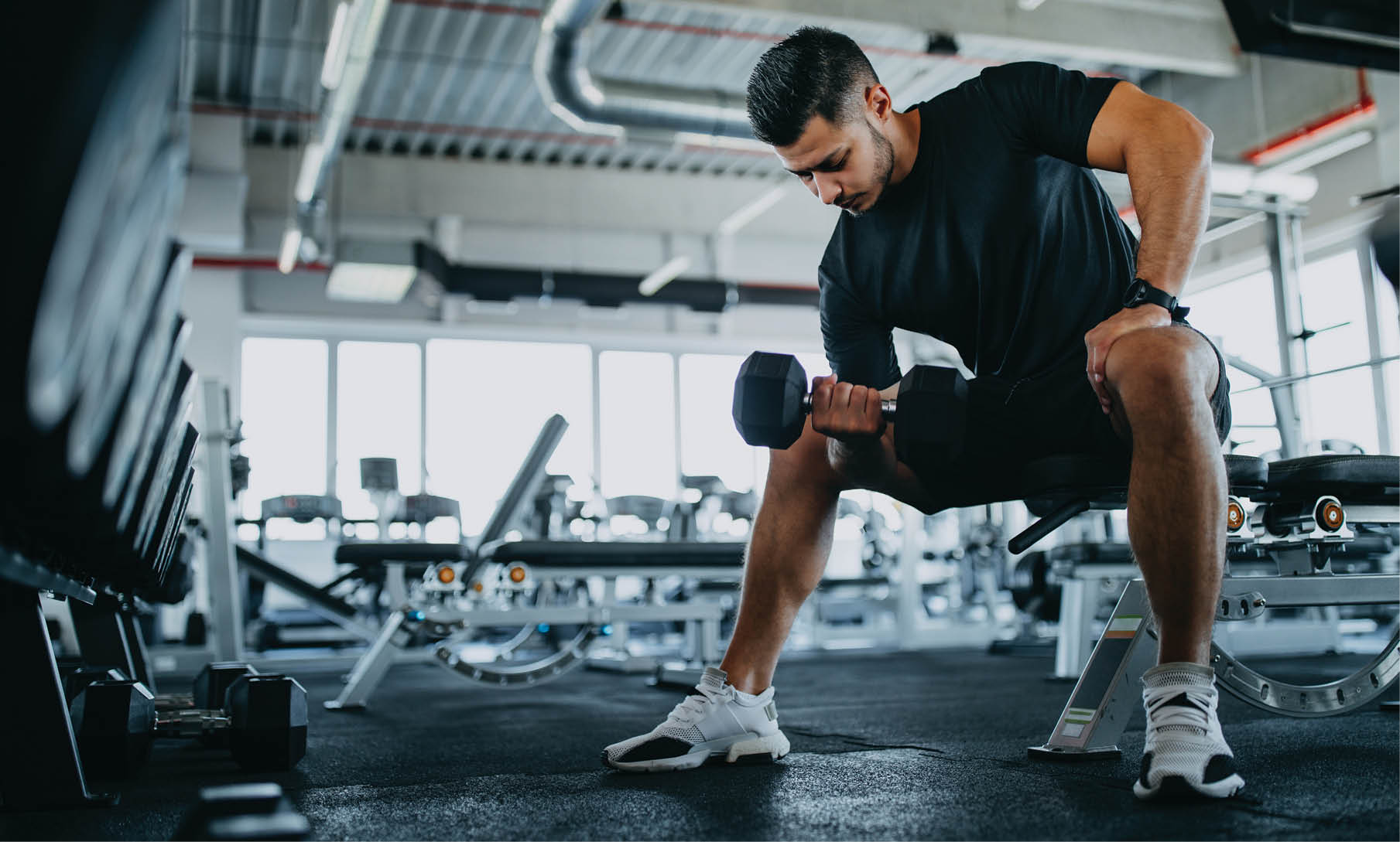 Man sitting on one gym machine and doing biceps.
