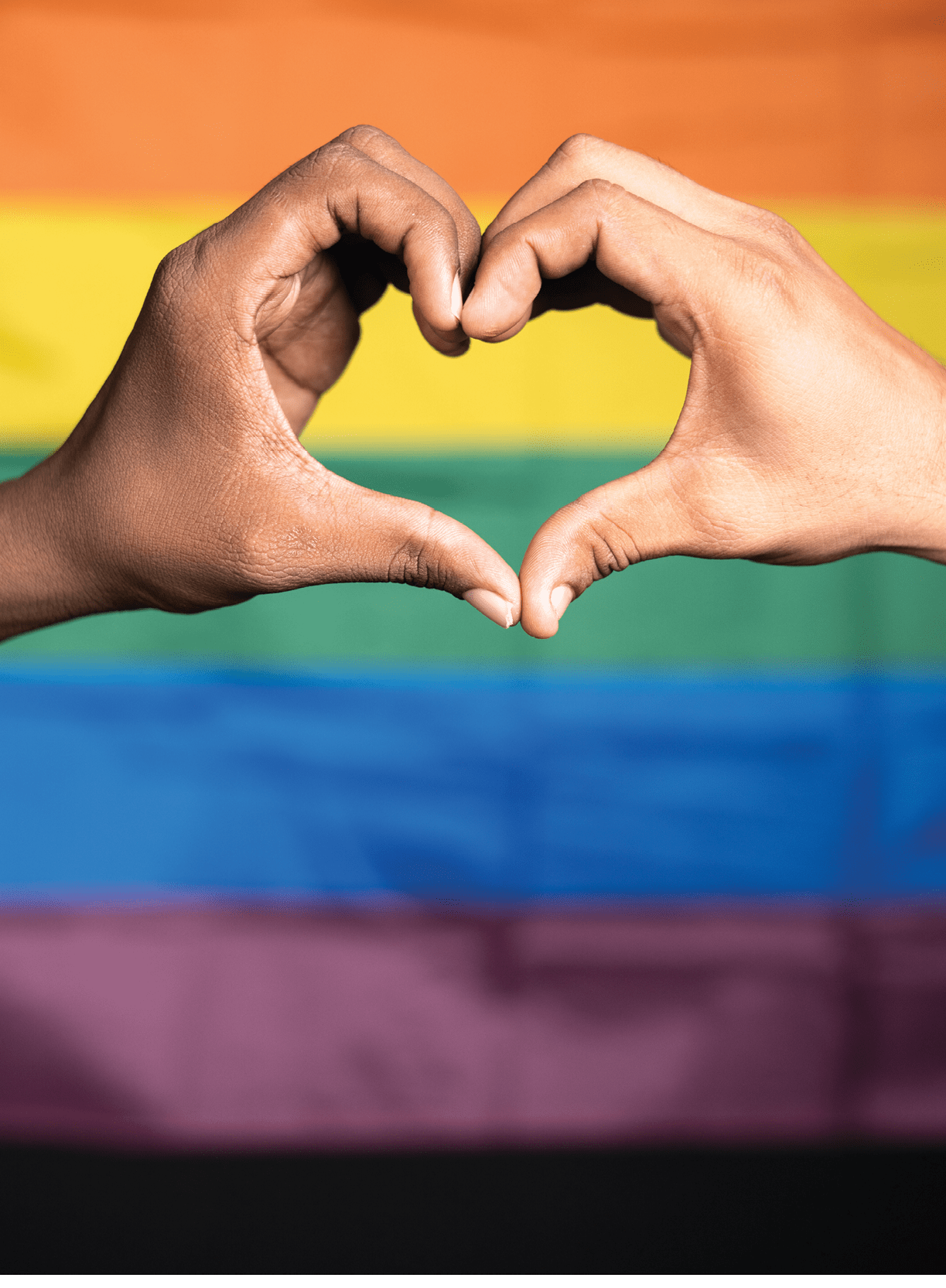 vertical close up shot of hands making love or heart symbol in front of pride or rainbow flag - concept of gay couple love, solidarity and pride month celebration